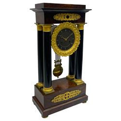 French - Napoleon III 8-day Portico clock in a rosewood and ebony case with circular turned pillars and cast brass capitals, with a flat top and stepped base raised on brass button feet, movement and dial suspended in a gilt drum case with a cast bezel, slate dial with incised roman numerals and gilt moon hands, with a visible gridiron compensated pendulum and brass faced bob, twin train countwheel striking movement, striking the hours on a bell. 