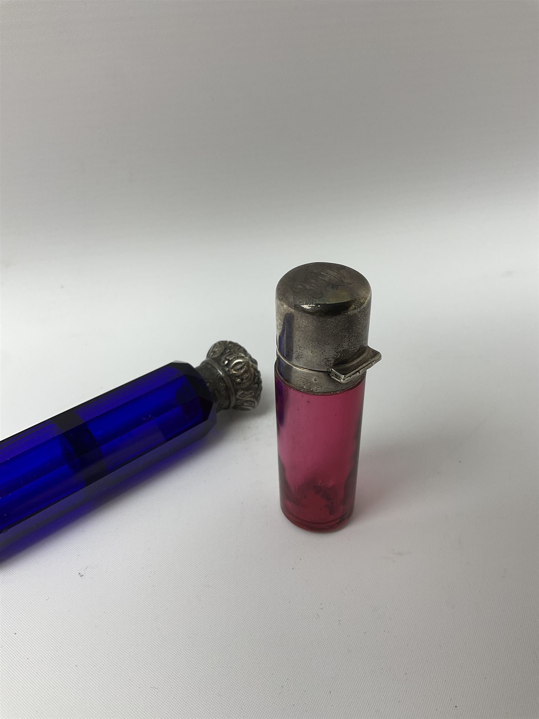 Late Victorian silver mounted ruby glass cylindrical scent bottle, with interior glass stopper, Birmingham 1900, makers mark worn, H8cm, together with a Victorian double ended cut blue glass perfume bottle mounted with white metal screw and flip caps decorated with foliate repousse detailing, H13.5cm