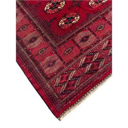 Afghan Bokhara red ground carpet, the field decorated with four rows of Gul motifs interspersed with Hac motifs, the border with lattice pattern panels within small geometric guard stripes, geometric patterned end panels
