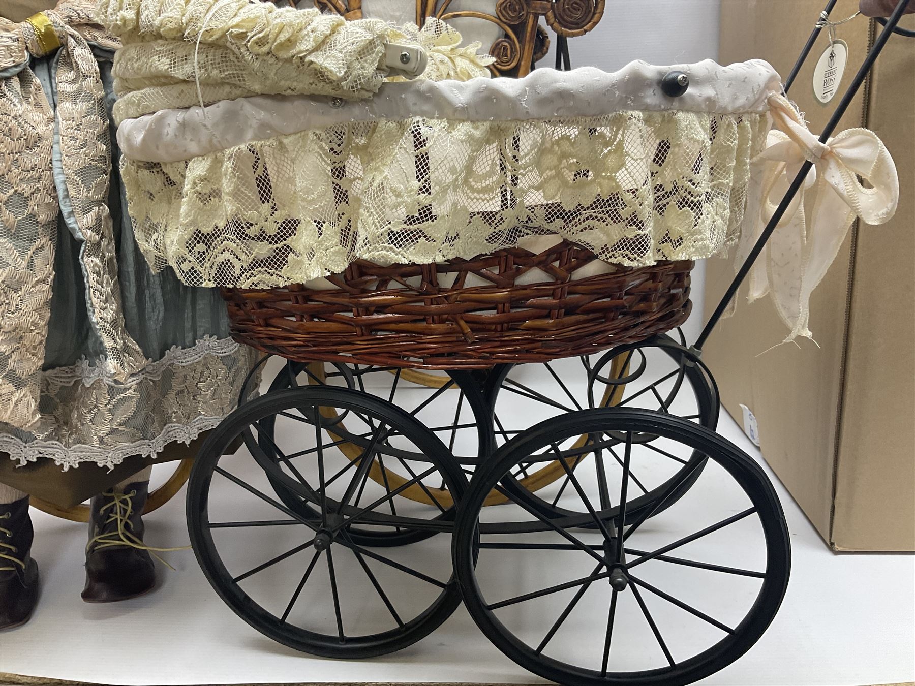 Two decorative wicker dolls prams, one with lace parasol,  and eleven dolls, including Leonardo Collection porcelain dolls, tallest pram including parasol H105cm