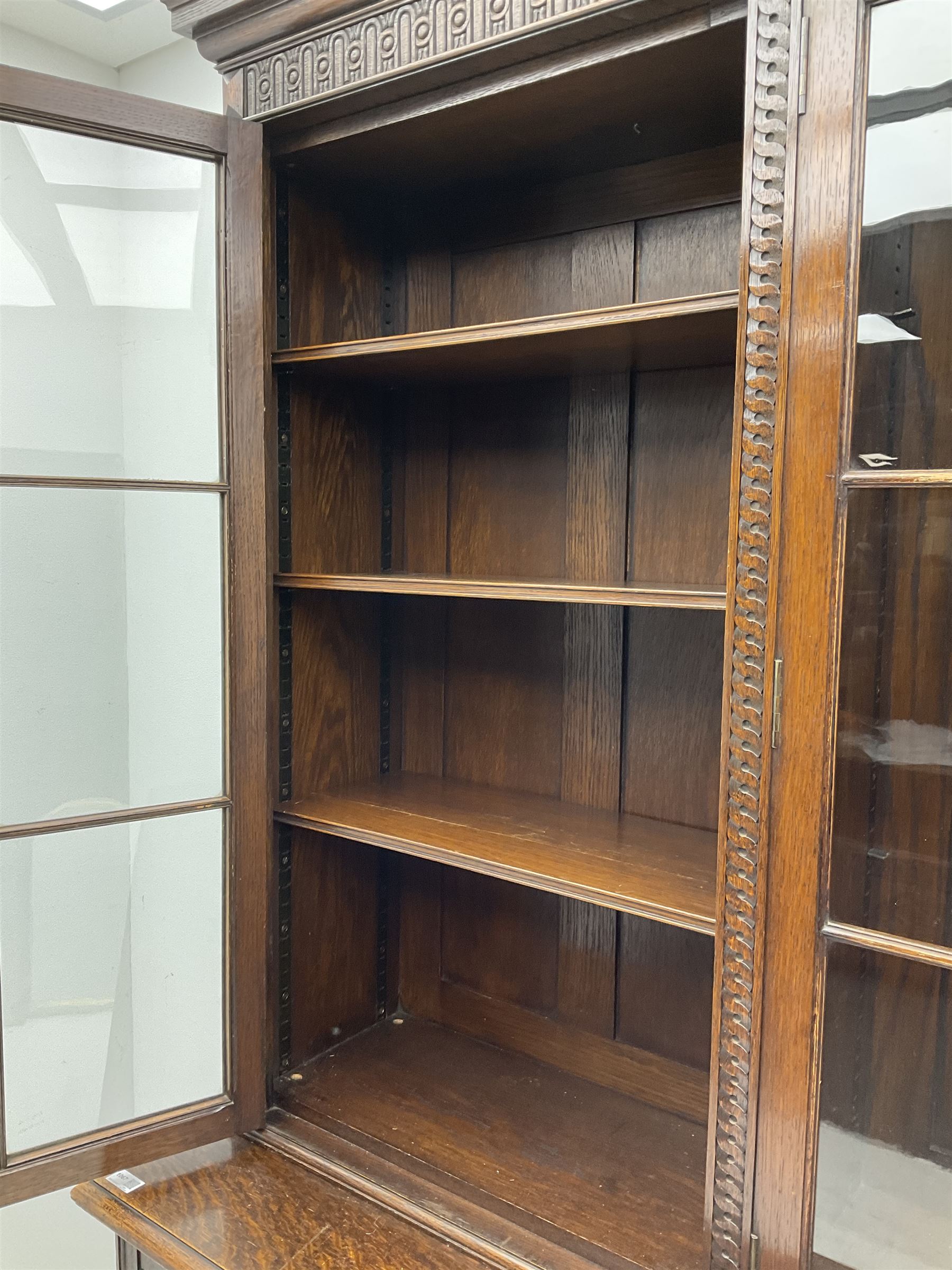 Waring and Gillow - oak bookcase on cupboard, projecting cornice over arcade frieze, guilloche upright decoration, the top section enclosed by three astragal glazed doors, the lower section enclosed by three geometric panelled doors with blind fretwork decoration, on turned feet