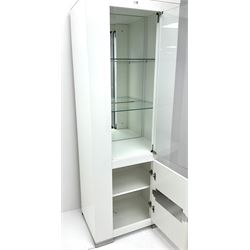 Gloss white illuminated display cabinet, single door enclosing two glazed shelves above cupboard on metal supports 