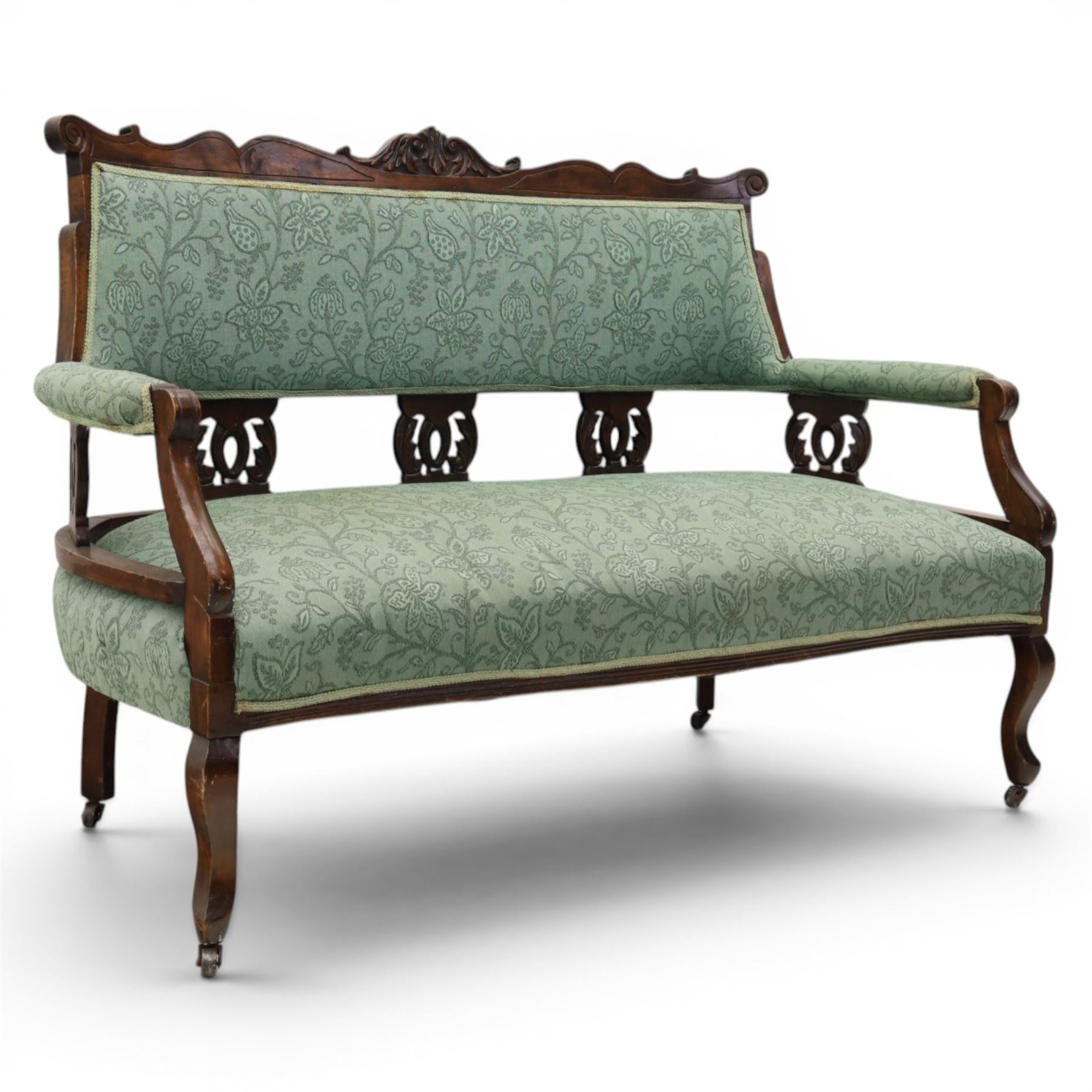Edwardian mahogany framed sofa, shaped cresting rail with scroll terminals and carved foliate pediment, upholstered back and swept arms in green foliate fabric, pierced splat supports, serpentine front seat rail, on cabriole supports terminating in castors