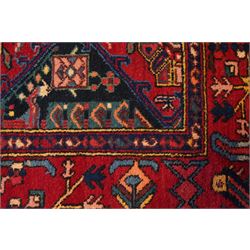North West Persian Heriz hand-knotted rug, madder red field with an all-over lattice of stepped lozenge medallions enclosing stylized geometric floral motifs and ivory reserve panels, framed by angular vinery and motif borders, main border with with stylized rosettes and geometric devices, flanked by narrow guard stripes,, cotton fringe ends 