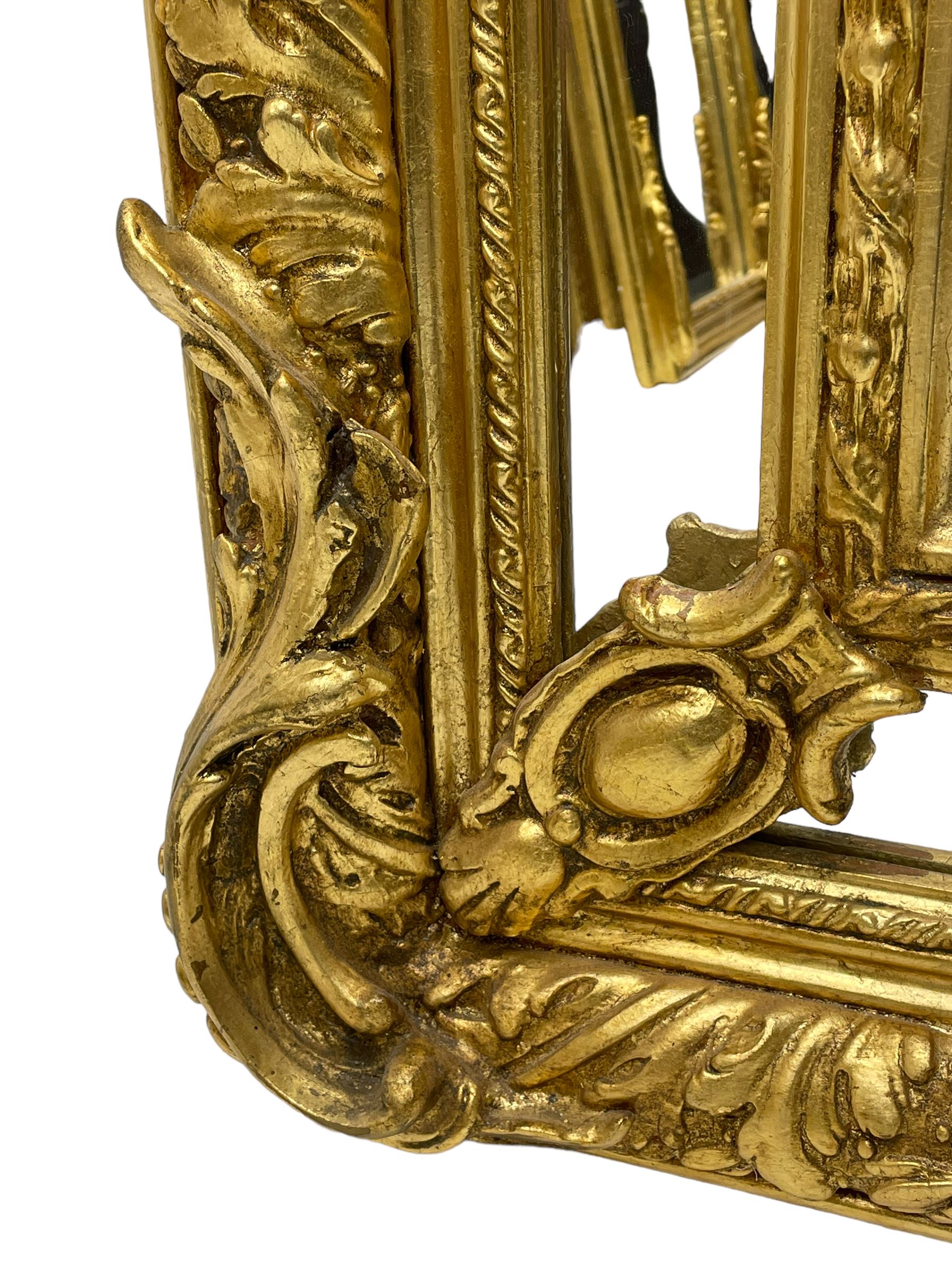 Large Italian Baroque design gilt wall mirror, the shell pediment over circular panel depicting classical female flute player with dancing putto within a tree landscape, the stepped arched upper frame surmounted by musical instrument playing putto and trailing flower heads, central bevelled mirror plate surrounded by plain segmented mirror plates, acanthus leaf moulded outer frame and foliate moulded inner slip