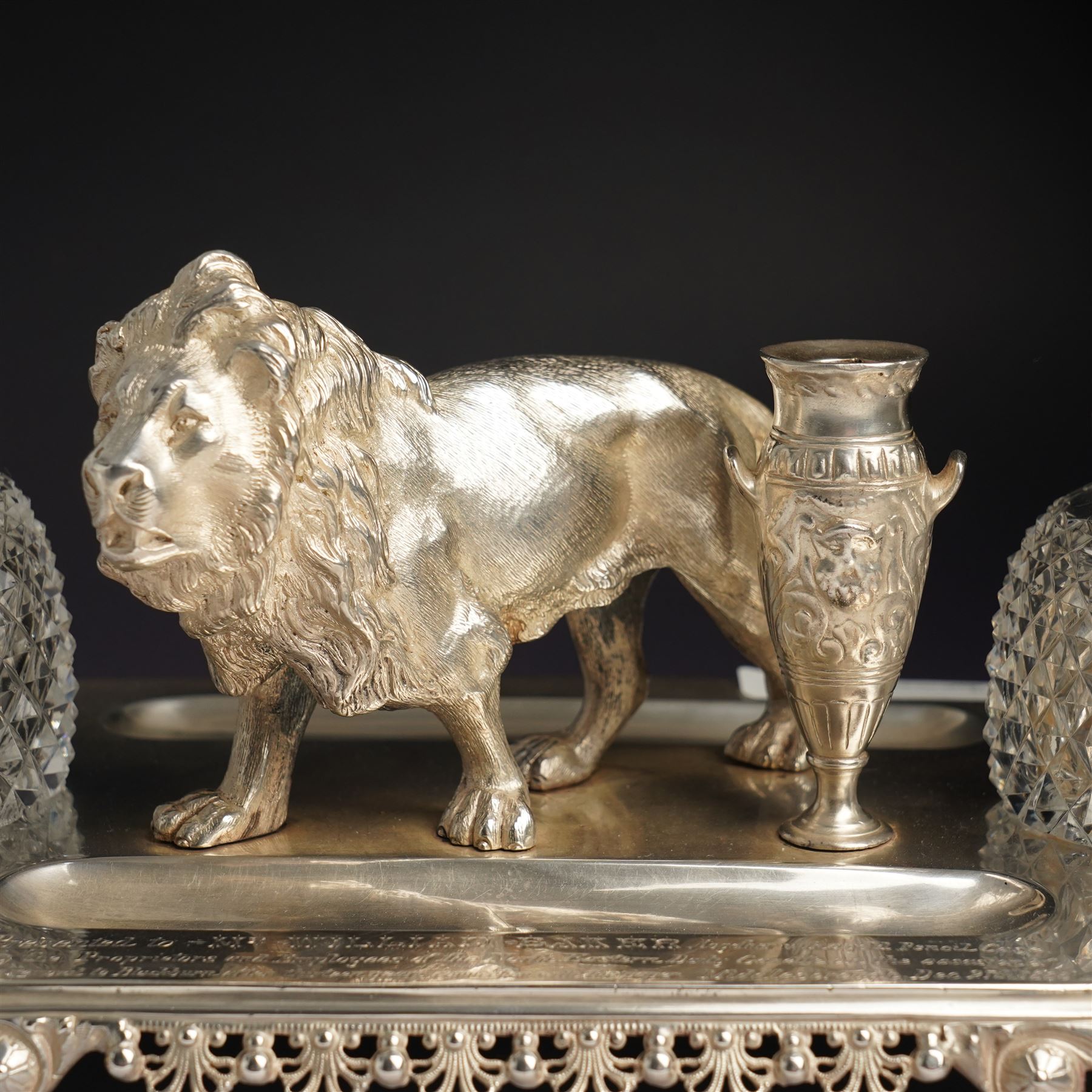 19th century Walker & Hall, silver plated inkstand, oblong and on four paw feet, the border decorated with pierced shell design, each side with a pen-rest, with two cut-glass bottles and central lion and urn finials, engraved to the front with an inscription, H15cm, L30cm