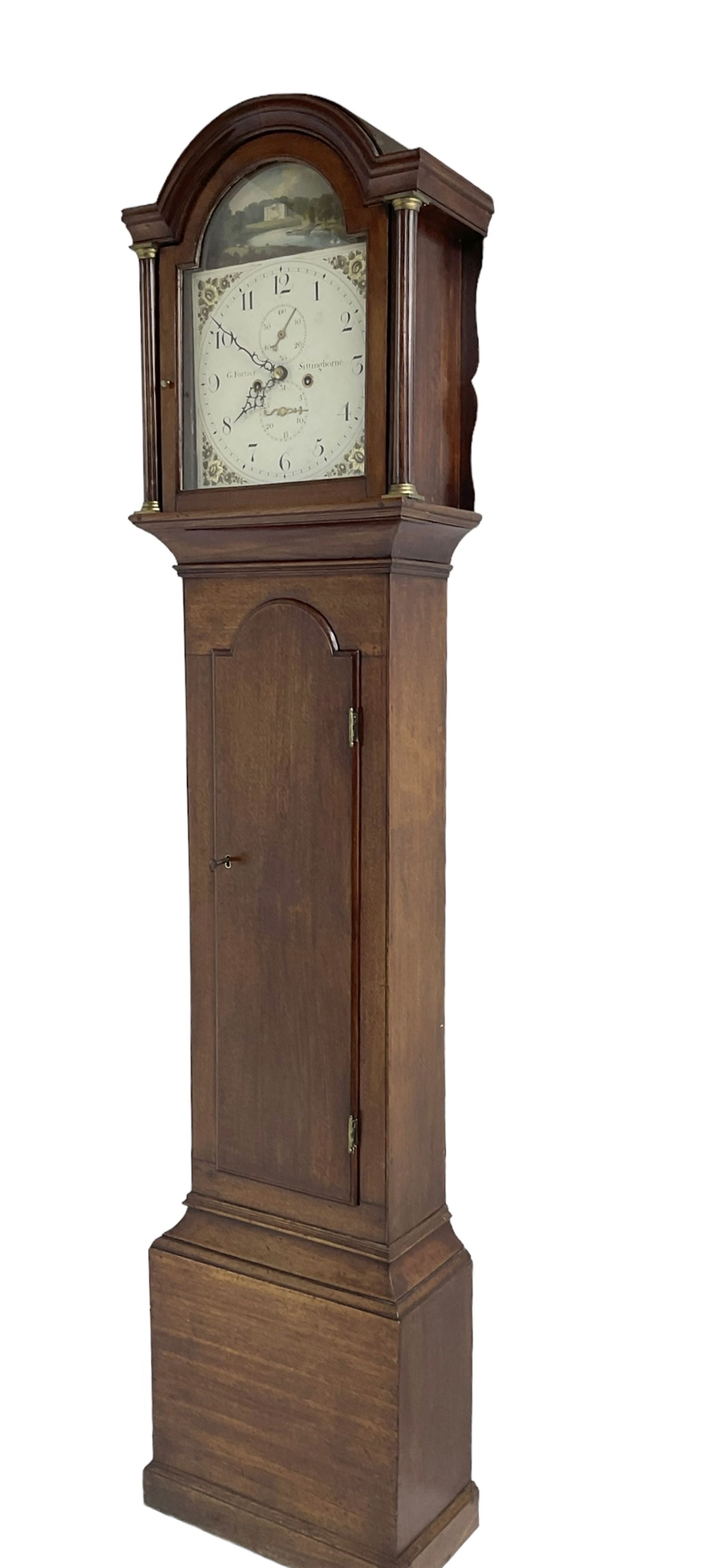 G Fortier of Sittingborn - Early 19th century 8-day mahogany longcase clock c1825, with a break arch pediment and hood door flanked by reeded pilasters with brass capitals, plain case with a long trunk door with a conforming break arch top, plinth with applied skirting, painted dial with upright Arabic numerals, date  and seconds dials, floral spandrels and a rural depiction of a country house and river to the arch, replacement steel hands with brass pointers to the calendar and seconds dials, dial pinned directly to a rack striking movement. With weights, pendulum and winding key.