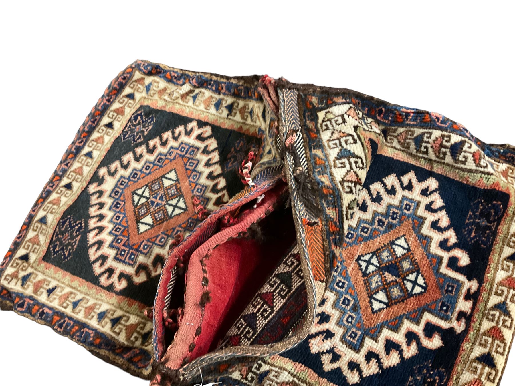 Antique Persian red ground saddle bag, decorated with all-over Boteh motifs, geometric patterned border (127cm x 68cm); Persian indigo ground saddle bag, decorated with two geometric ivory lozenges (113cm x 62cm); Persian red ground saddle bag decorated with lozenges and multi-band border (110cm x 65cm) 