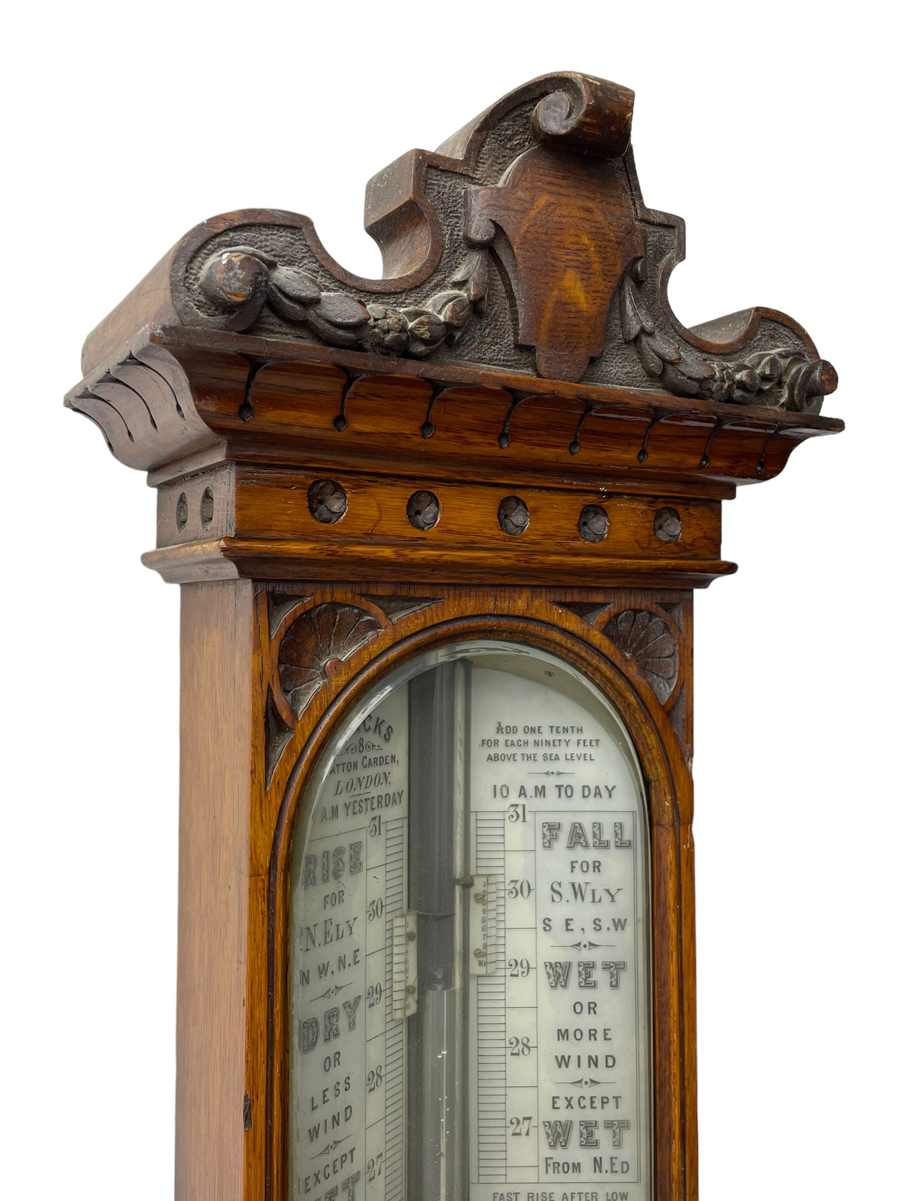 J Hicks - Hatton Garden London, - late 19th century carved oak cased Fitzroy barometer in a richly carved case with a carved crested pediment and square cistern cover, inverted opaline register reflecting FitzRoy's predictions and a scale from 27 to 31 inches of barometric pressure, with a thick bore cistern tube and adjustable rack and pinion twin vernier, fitted with a glazed snail bulb mercury thermometer recording the air temperature in both Fahrenheit and Celsius. Mercury clean and present.
James Joseph Hicks was born in Ireland, however, early in his life he moved to London where he was apprenticed to the instrument maker Louis P Casella. In 1860 he went into business in his own right as a scientific instrument maker at 8 Hatton Gardens. In 1864 he was granted membership to the British Meteorological Society and exhibited instruments at the Royal Society Exhibitions between 1876 and 1913. Hicks was one of London's most prolific and eminent barometer makers. 