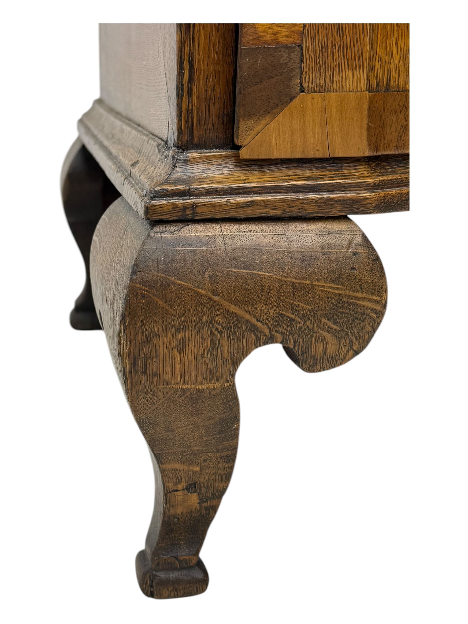 Late 19th century continental oak commode, serpentine fronted with parquetry and crossbanded decoration, the raised superstructure back fitted with a central bank of five recessed drawers flanked by concave drawers, above three full-width drawers with brass ring handles, raised on cabriole supports