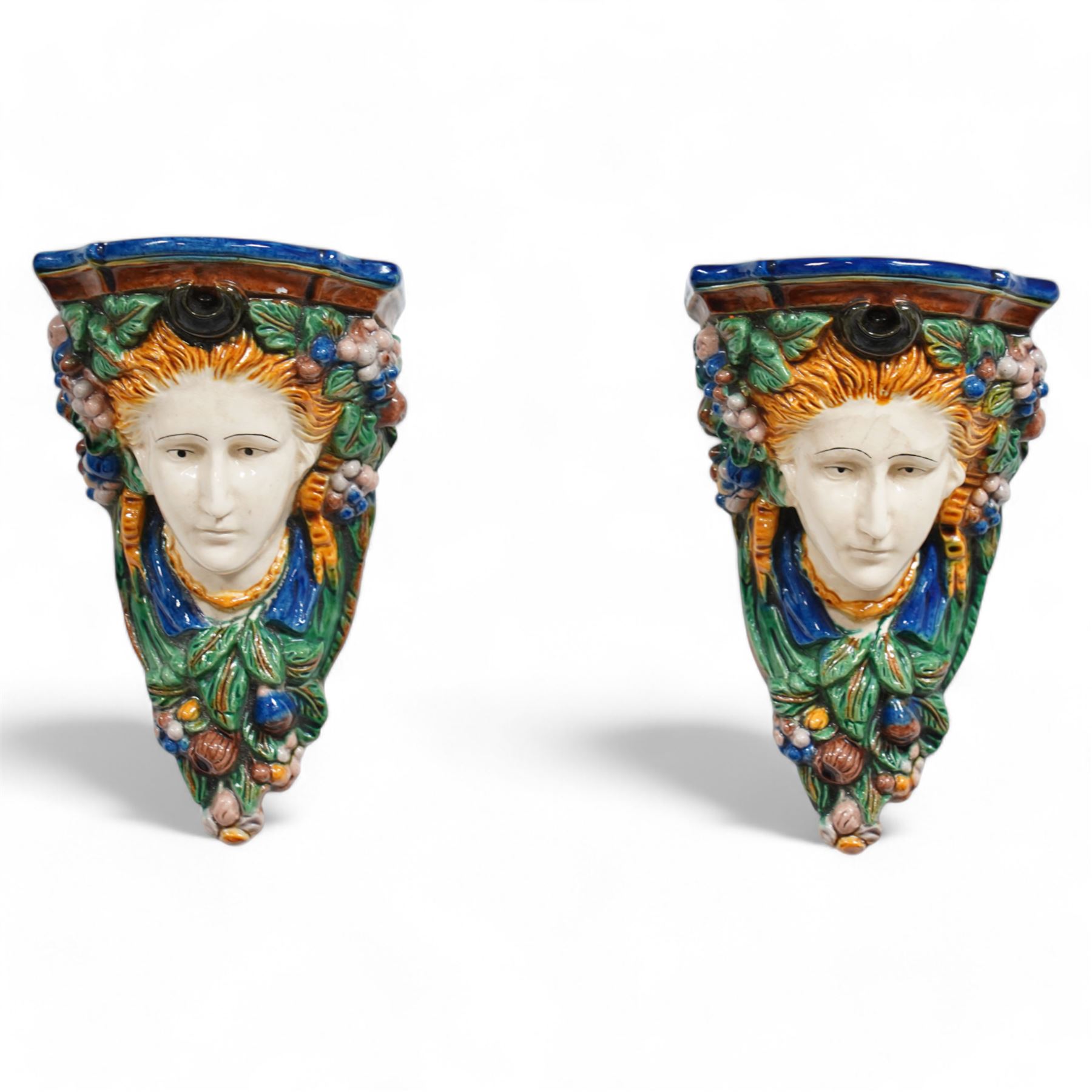 Pair of early 20th century Majolica wall brackets or corbels, formed as two ladies in high relief surrounded by fruit and foliage, on a blue and green ground H30cm 