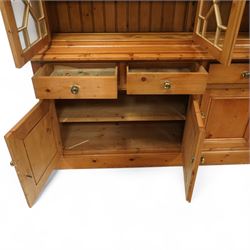 Mid 20th century pine glazed dresser on cupboard base, upper section of rectangular form with three astragal glazed hinged doors enclosing two adjustable wooden shelves and projecting frieze over three short drawers and three hinged panelled cupboard doors with brass handles, the front and sides, raised on a plinth base 