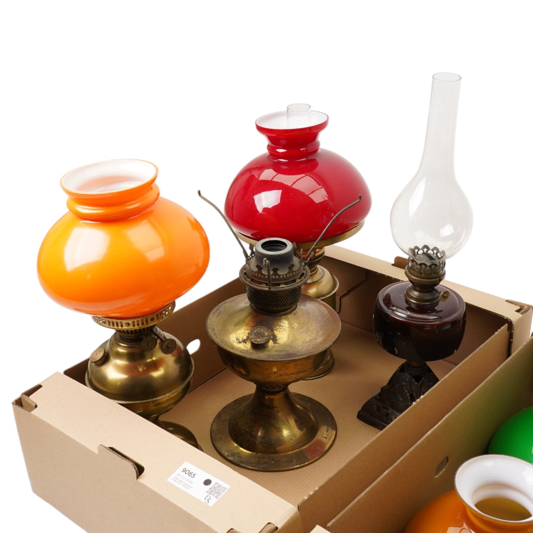 Table oil lamp with red glass reservoir on metal base, three other oil lamps and various shades and chimneys