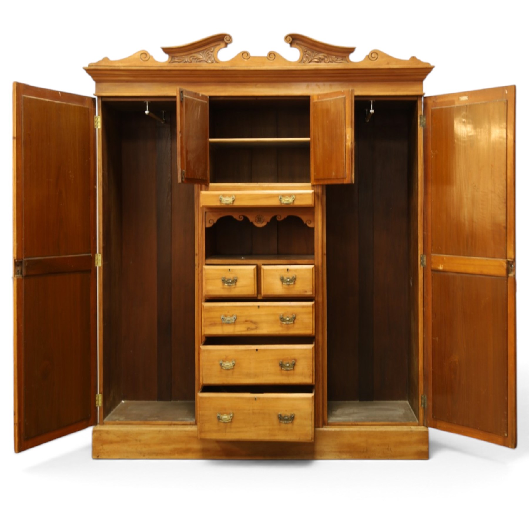 Edwardian walnut triple combination wardrobe, projecting pediment with pierced foliate scroll cresting above a central cupboard flanked by bevelled mirrored doors, over open recess with mirrored back, above two short and three long drawers with brass handles, interior fitted with hanging rails and shelf, raised on plinth base