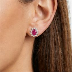 Pair of 18ct white gold ruby and diamond earrings, each stud set with a single oval cut ruby and surrounded by ten round brilliant cut diamonds, stamped, total ruby weight approx 1.40 carat, total diamond weight approx 0.60 carat
