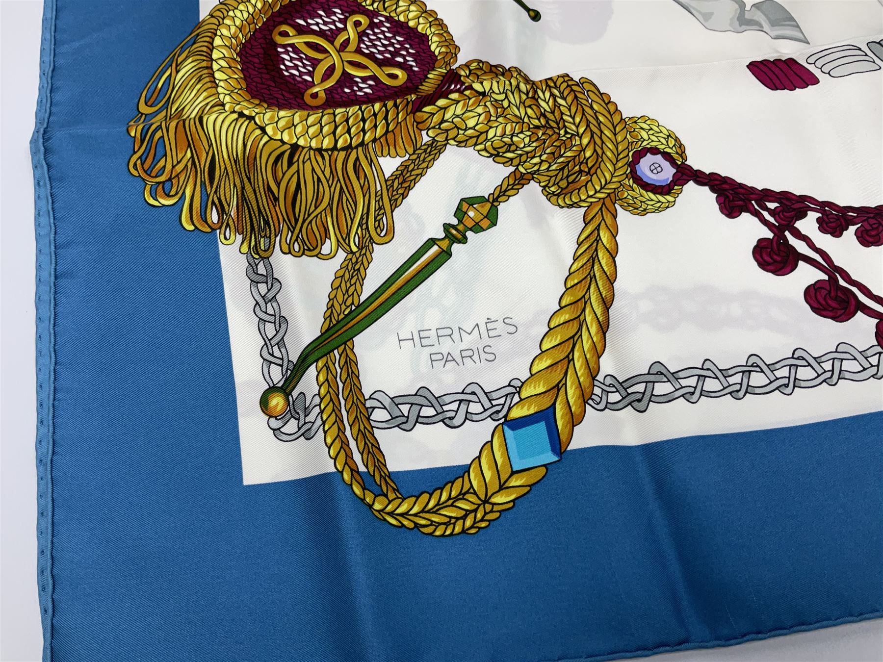 Hermès 'Le Timbalier' silk scarf, designed by Francoise Heron in 1961, printed with a central image of a gentleman on horseback donning extravagant dress, on white ground surrounded with colourful stylised knotted ropes, contained within peacock blue border, with rolled hand stitched edges and Hermes material label, 87cm square