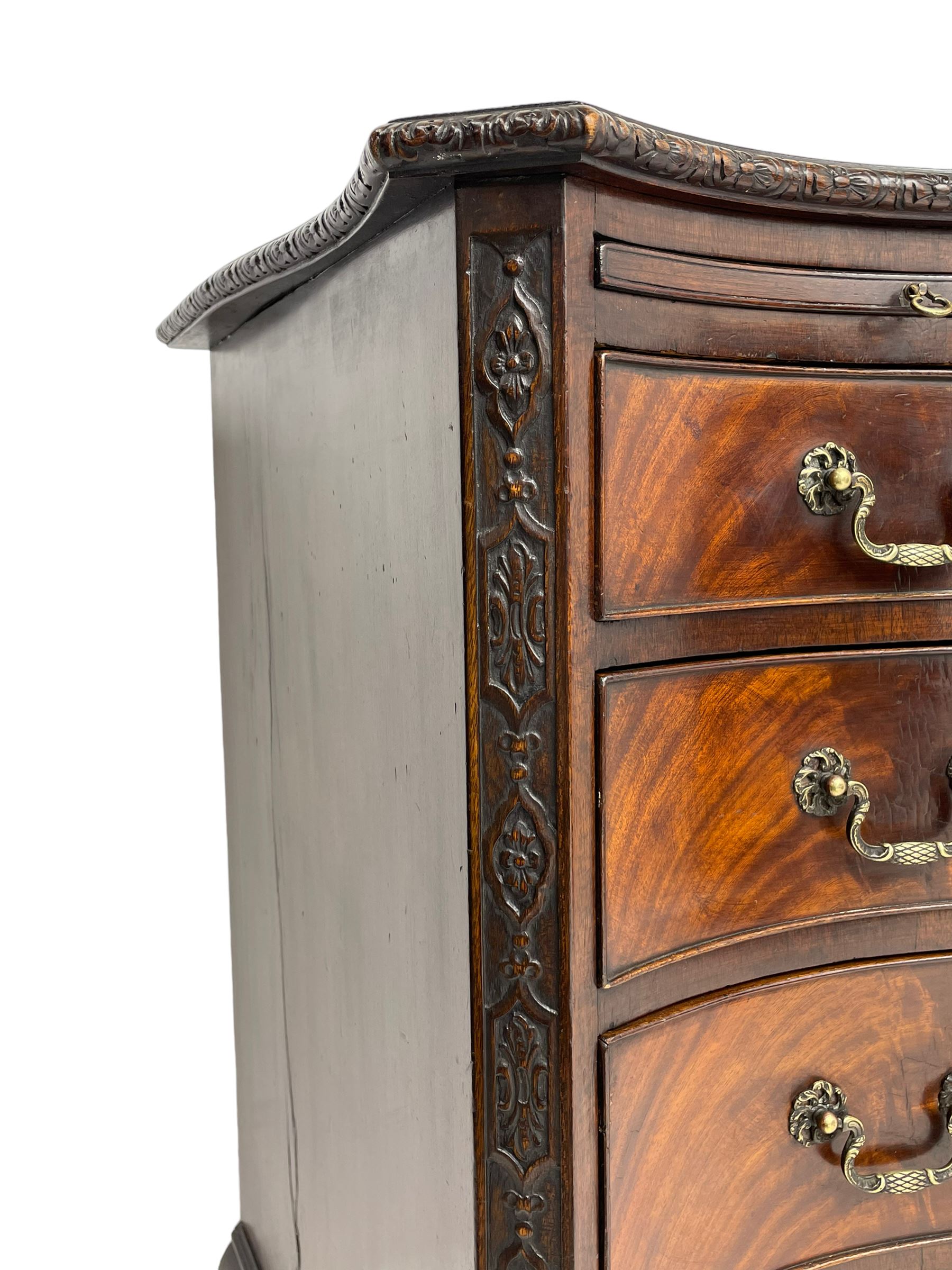 Chippendale design serpentine chest, shaped moulded top carved with repeating flower head motifs, fitted with brushing slide over four graduating drawers, pierced and foliate moulded handle plates with scrolled swan neck handles, canted upright corners carved with flower heads and strapwork, on canted ogee bracket feet