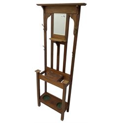 Edwardian oak hall stand, raised back with rectangular bevelled mirror plate surrounded by shelf and coat hooks, fitted with a glove box with hinged lid, over an undertier with two inset umbrella drip trays