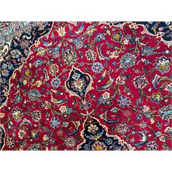 Persian Kashan crimson ground carpet, the central pole medallion decorated with flower heads, surrounded by trailing leafy branches and palmettes, scrolling border decorated with further palmettes, within floral pattern guard stripes 