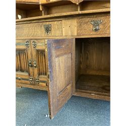 Shapland and Petter - Arts & Crafts period oak dresser, raised gallery top with spade balustrade, central bevelled mirror flanked by two cabinet, astragal glazed doors with yellow tinted glass and bullseye panes, the sides with pierced heart shaped decoration, fitted with two drawers and two double cupboards, enclosed by linenfold panelled doors,  copper work strap hinges and fixtures, on shaped spade feet, the locks stamped 'S&P'