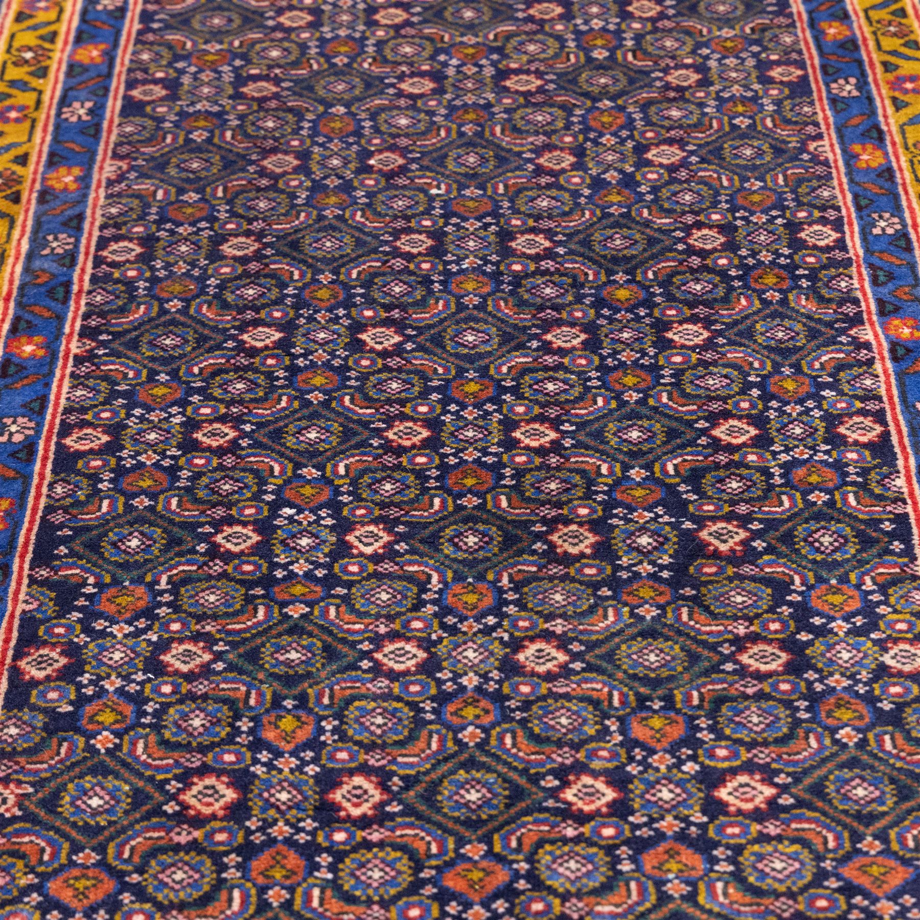 North West Persian Bidjar hand-knotted runner, decorated with an all-over herati pattern on a deep indigo ground, the field is filled with a repeating diamond and rosette motifs, interspersed with stylized leaves and floral elements, framed by a border on an ochre ground flanked by contrasting guard borders, with cotton fringe ends 