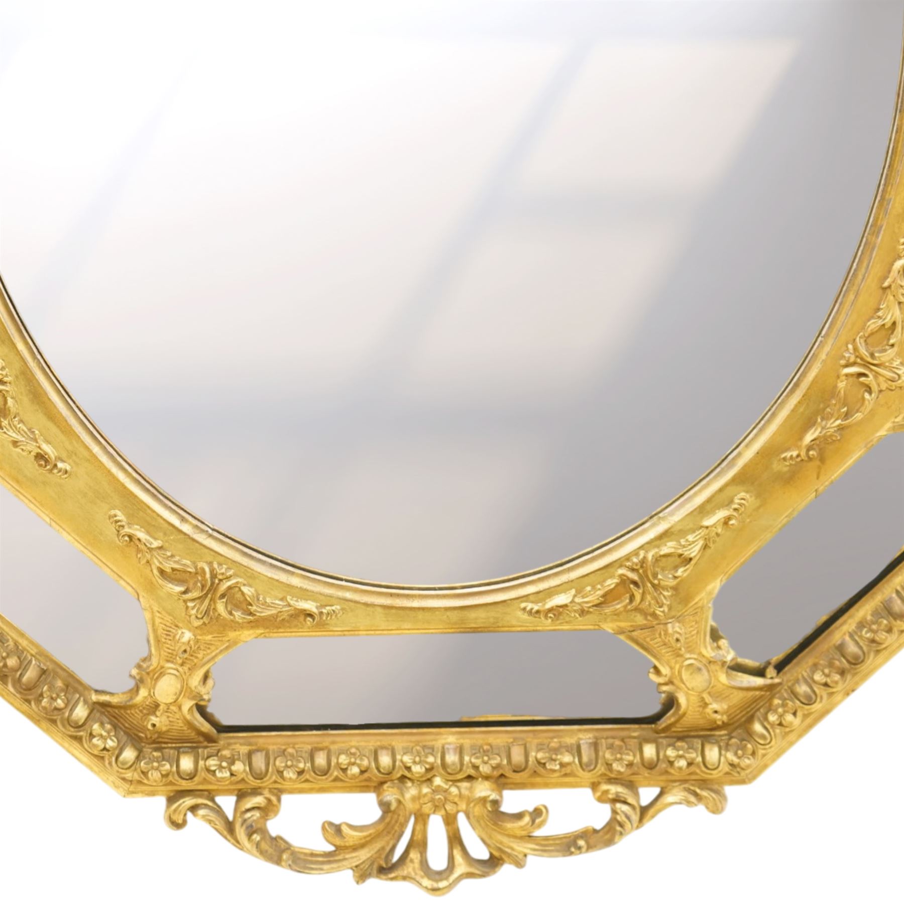 Late 19th century French giltwood and gesso wall hanging cushion mirror, the pierced foliate rocaille pediment extending acanthi C-scrolls and trailing bellflowers, over a floral garland and cartouche moulded rails, the central oval bevelled plate surrounded by further bevelled cushion mirrors, with out-scrolling pierced motifs flanking the floral egg-and-dart moulded outer edge, over a pierced foliate cartouche terminal