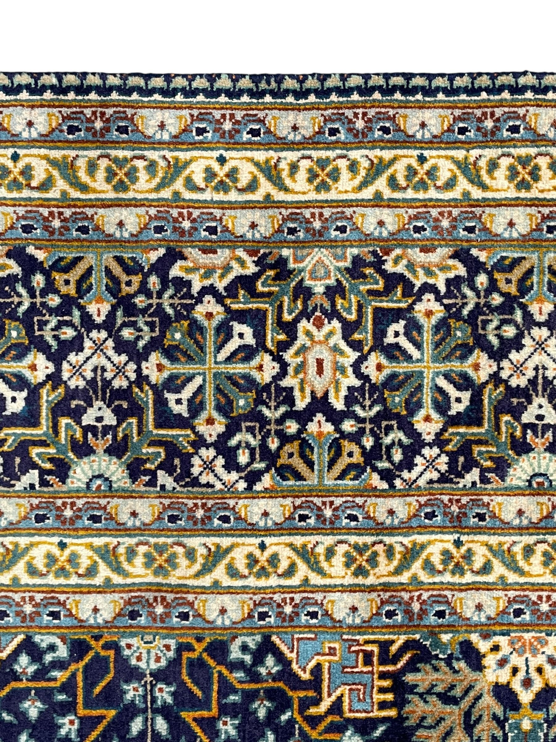 Persian indigo and pale gold ground rug, overall busy geometric design, the field decorated with hooked Hac and palmette medallions surrounded by densely patterned zig-zags and stylised foliate motifs, the border decorated with smaller Hac motifs, within multiple guard stripes 