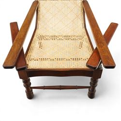 20th century teak framed plantation chair, plain cresting rail over cane back and seat, fitted with hinged extending leg rests, raised on turned front-supports united by ring-turned stretcher