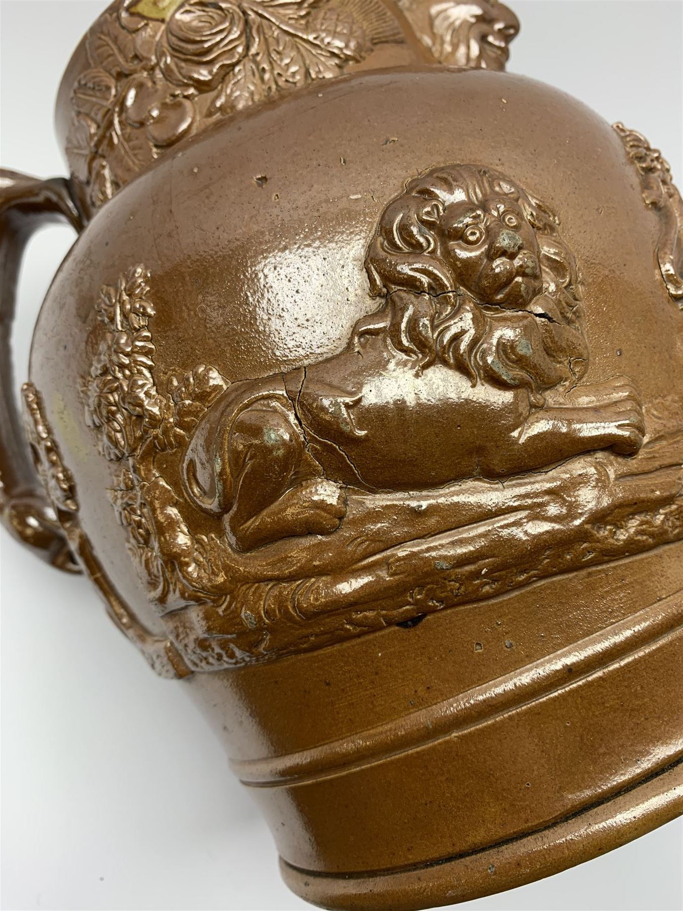 19th century salt glazed stoneware jug, with mask spout and greyhound modelled handle, the body decorated in relief with Royal Coat of Arms flanked by lions, the rim with the flowers of the union, roses, thistles and shamrocks, H26.5cm
