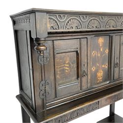 18th century and later oak court cupboard, lunette carved frieze over panelled front enclosed by two doors, inlaid with floral urn and two chequered lozenges, carved masks over tapering supports carved with feather decoration on lower tier, turned feet