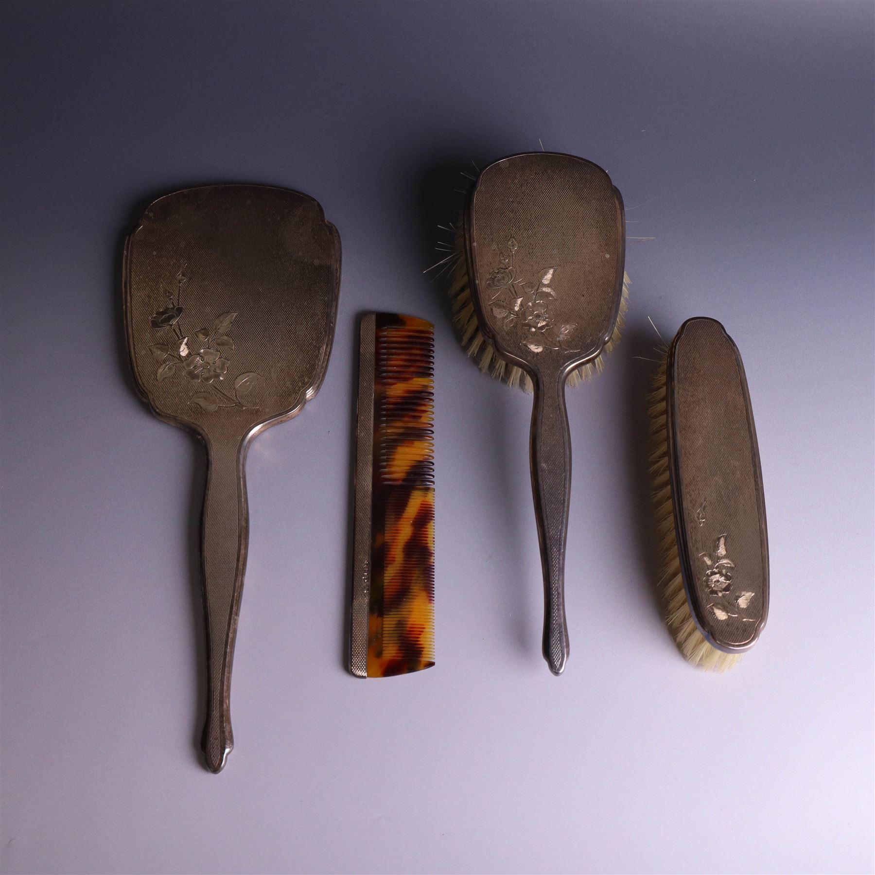 20th Century silver mounted dressing table set, comprising hand mirror, clothes brush, hairbrush and comb holder, each with engine turned and engraved floral decoration, three pieces hallmarked Adie Brothers Ltd Birmingham 1964, the comb holder hallmarked Elkington & Co Ltd Birmingham 1965, contained within a fitted tooled leather case