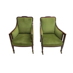 Pair Edwardian mahogany framed armchairs, with satinwood stringing, foliate carved cresting rail, upholstered in green fabric with sprung seat, raised on square tapering supports with spade feet and brass castors