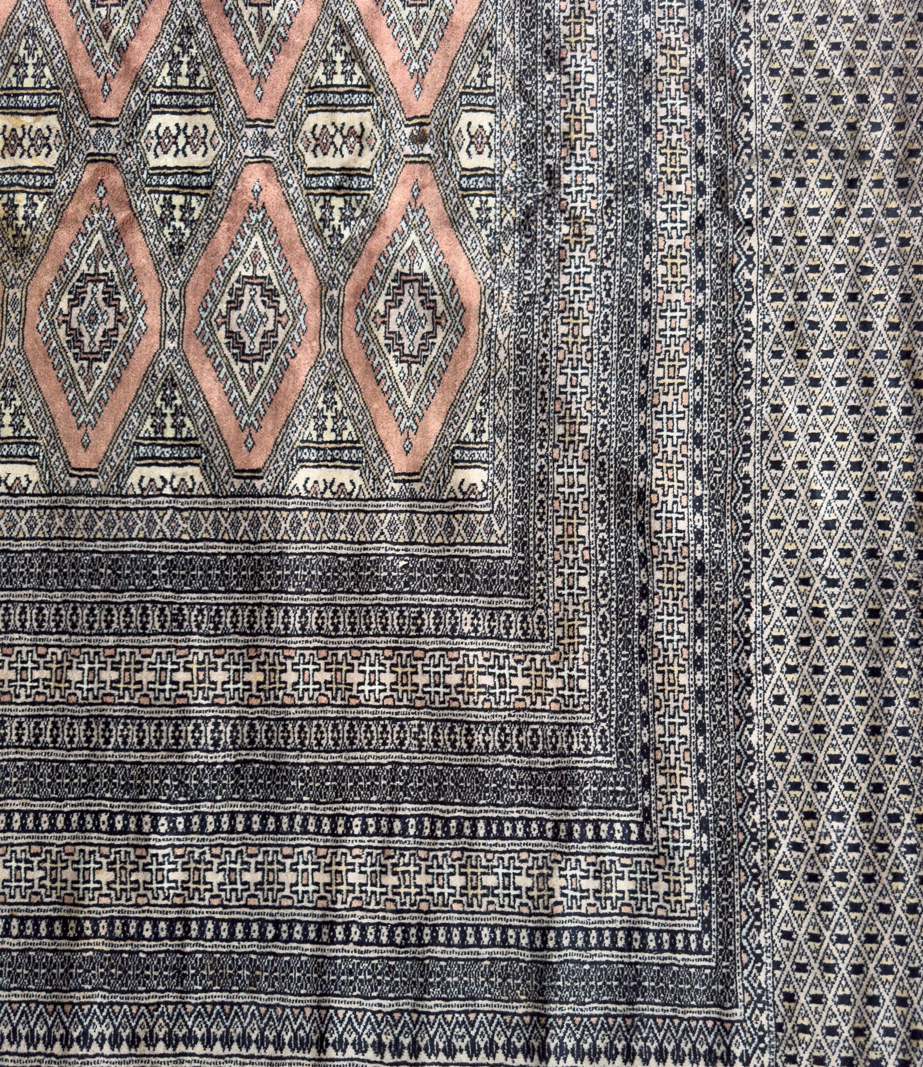 Large Persian Bokhara wool rug, the field decorated with repeating gul motifs in lozenge medallions across a dark ground, enclosed by multiple geometric borders in indigo, ivory and terracotta, from the region of Baluchistan