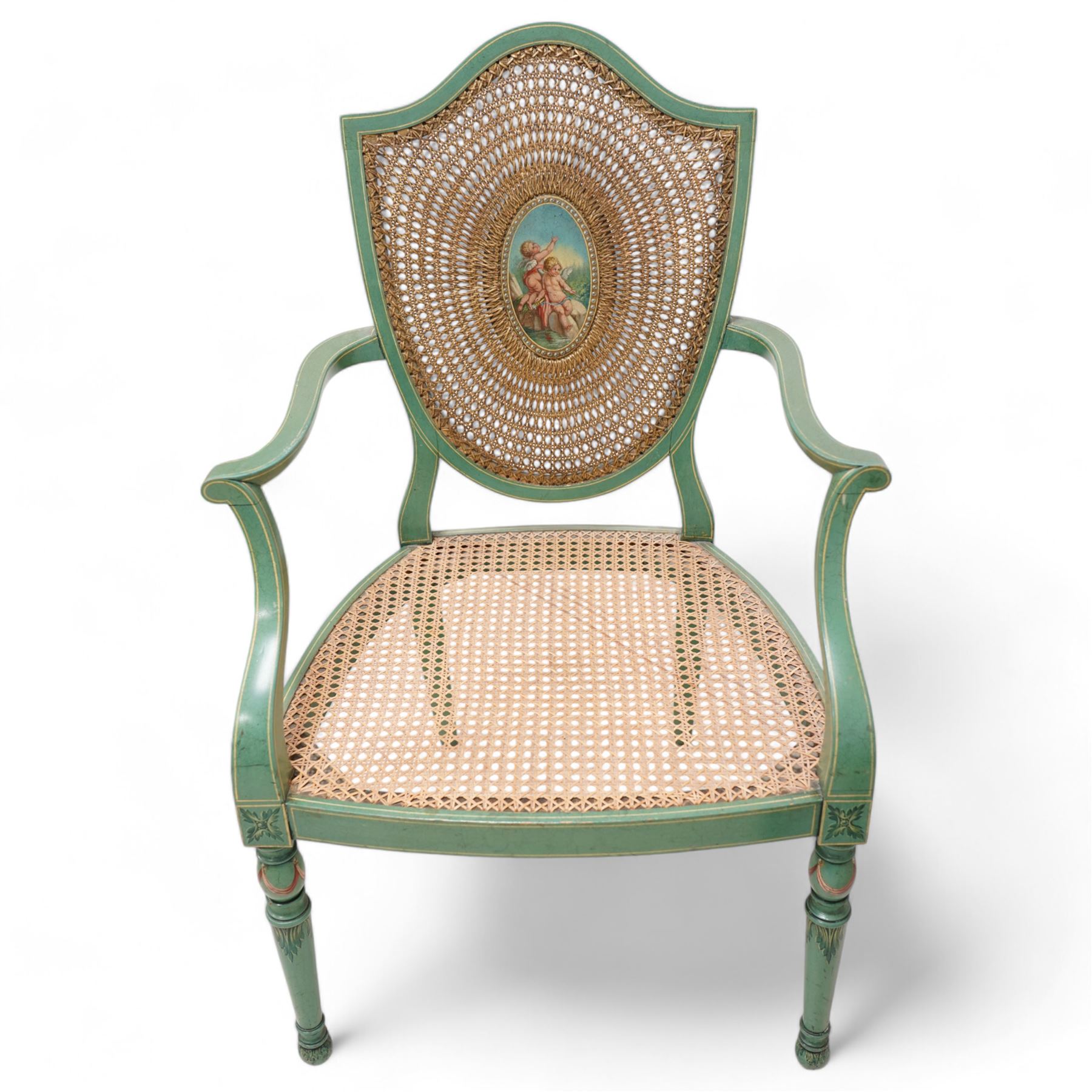 Pair of Edwardian Hepplewhite Revival green-painted open armchairs, cane work shield back with central oval panel panted with putto set upon rocky landscape with water and trees, shaped and rolled arms enclosing cane work seat, on turned front supports decorated with acanthus leaves and draped festoons 