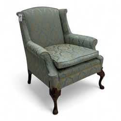 Georgian design carved walnut framed wingback armchair, upholstered in pale blue and gilt floral damask, with shaped loose seat cushion and rolled arms, raised on scallop and cartouche carved front cabriole supports terminating to pad feet