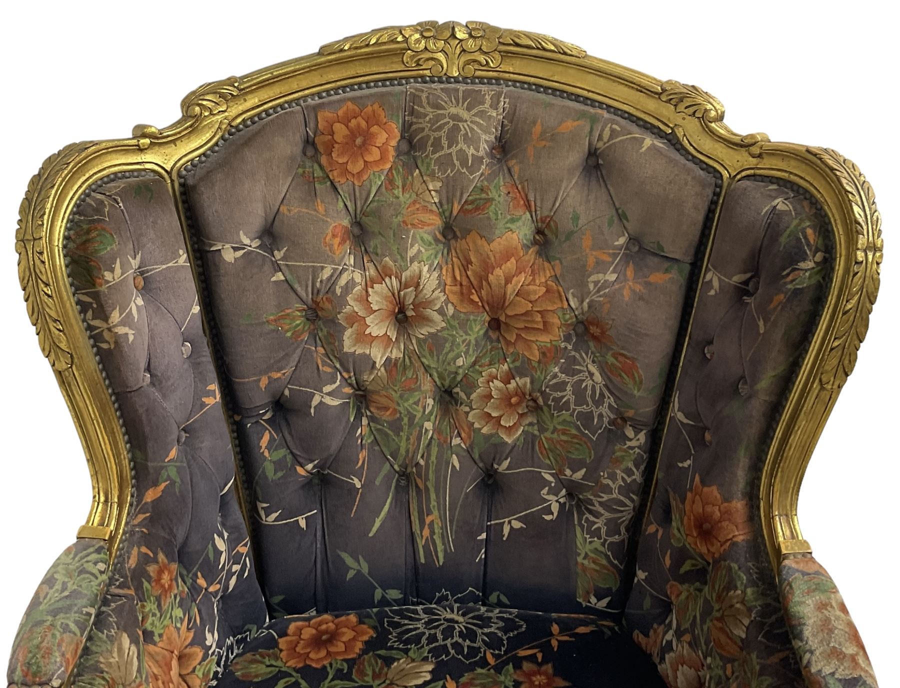 Pair of Louis XVI design gilt framed wingback armchairs, cresting rail carved and moulded with foliate decoration and C-scrolls, upholstered in buttoned floral patterned mauve velvet with loose seat cushion, scallop carved apron over cabriole supports