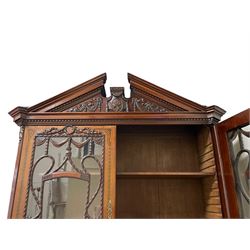 Large and impressive late 19th century Irish mahogany secretaire bookcase, moulded sloped arch dentil pediment decorated with central carved mask surrounded by linen festoons and trailing bellflowers, canted and fluted uprights with carved acanthus leaf upper and lower brackets, enclosed by two astragal glazed doors in the form of trophies with twist ribbon carved mouldings, inlaid with fanned spandrels and trailing leaf painted satinwood band, cylinder roll top inlaid with central fan motif and fanned spandrels, pull-out action revealing stepped fitted interior, central tambour roll cupboard flanked by two Composite pilasters and a combination of drawers and pigeon holes, fitted with three break-front drawers, matched canted and fluted corners with acanthus leaf carvings, on square tapering and fluted spade feet