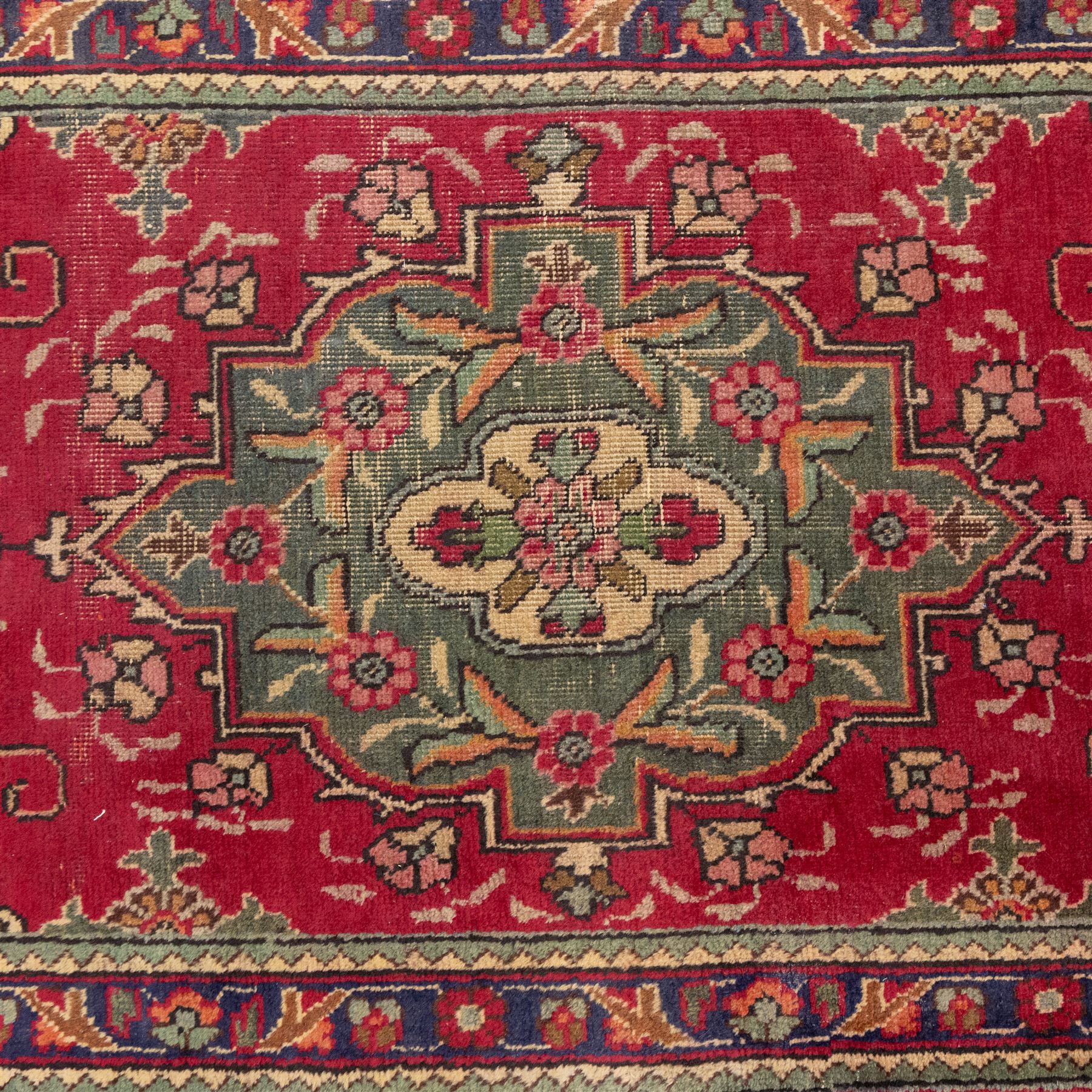 North West Persian Tabriz hand-knotted runner, madder red field with central octagonal medallions of sage green, navy and ivory, ground enclosing a floral rosette and radiating angular vinery, scrolling floral sprays and palmettes either end with shaped pendants principal border on navy ground decorated with a continuous vine-scroll of palmettes and rosettes, flanked by narrow guard borders, with cotton fringe ends 
