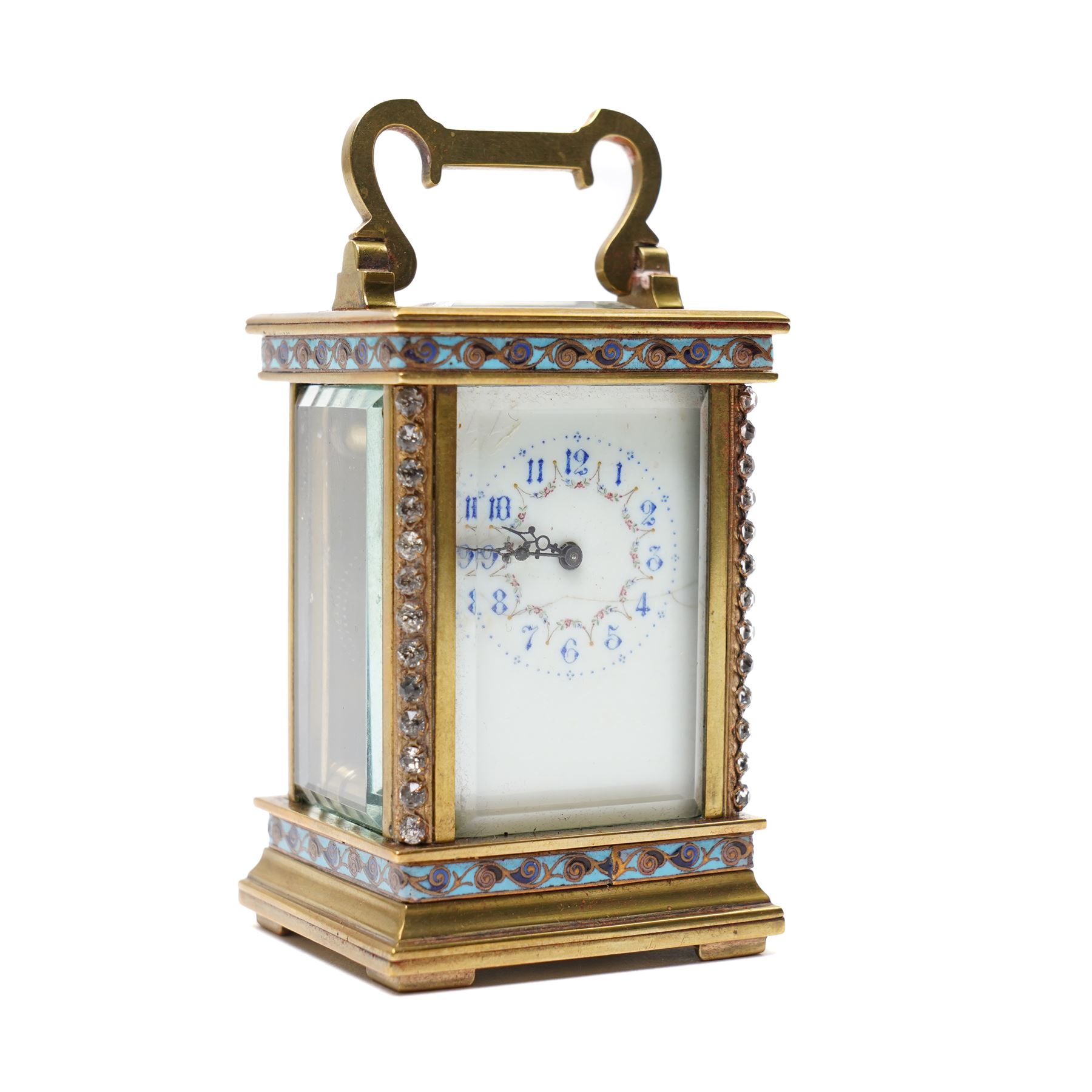 French- Edwardian miniature brass 8-day timepiece carriage clock with cloisonné panels to both base and cornice and paste gems to the front columns, decorative porcelain dial with a floral swag, blue Arabic numerals, minute track and pieced steel hands, square viewing glass to the top with a silvered lever escapement, with original leather bound traveling case.