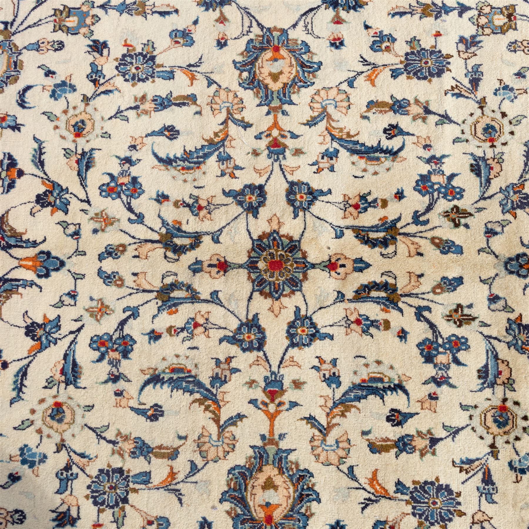 Large Central Persian Kashan hand-knotted carpet, ivory field with an all-over scrolling design of vines, palmettes, and floral sprays, enclosed by a broad camel-ground palmette and vine border, framed by multiple guard stripes in a palette of ivory, beige, blue and polychromed tones, with cotton fringe ends 