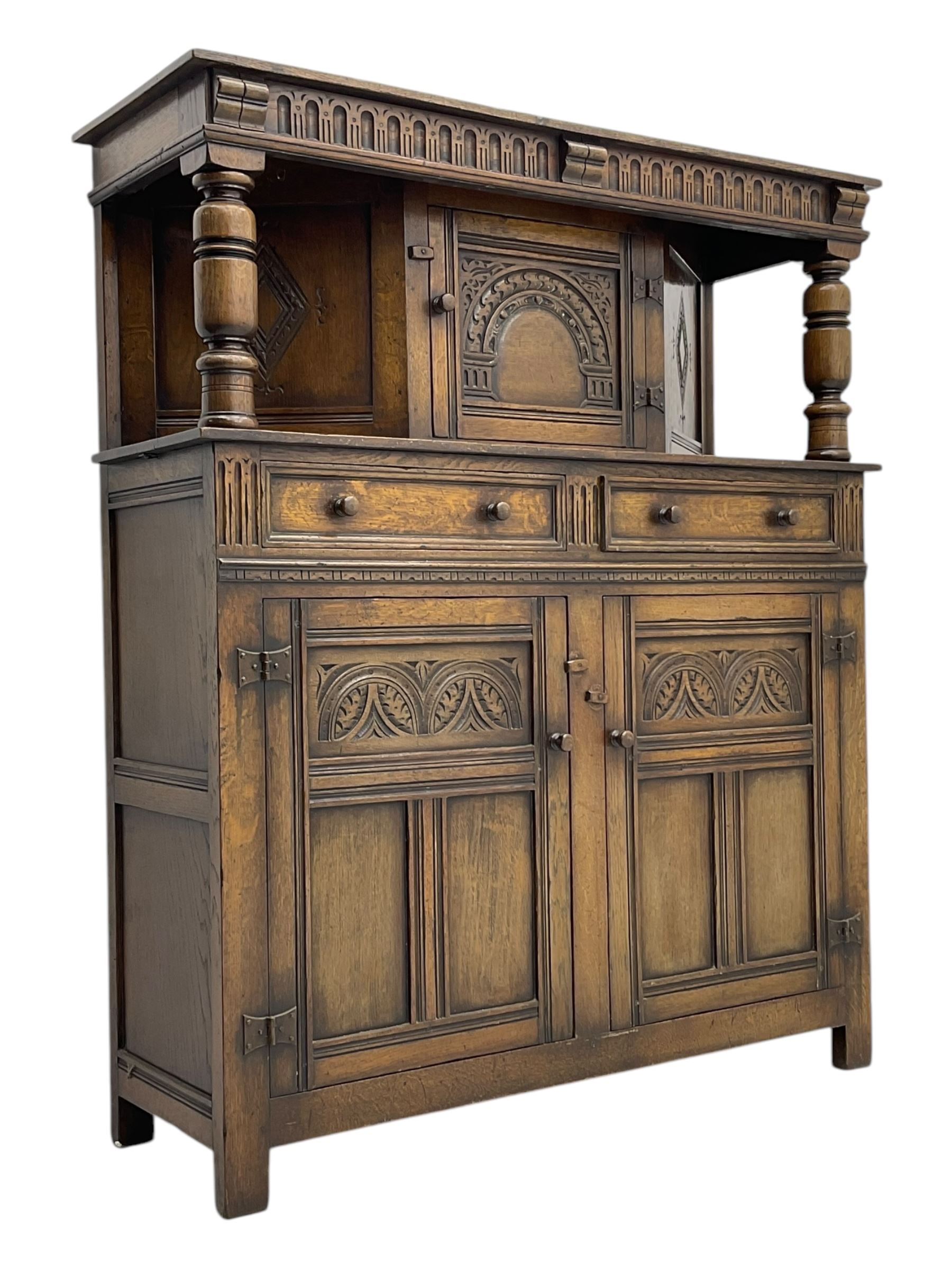 Jacobean design oak court cupboard, upper section with carved arched panelled cupboard door flanked by turned columns, beneath carved and moulded frieze, lower section fitted with two drawers over two cupboard doors with gothic arched panel decoration, raised on stile supports