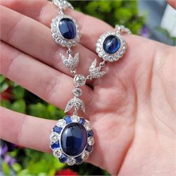 18ct white gold sapphire and diamond milgrain set necklace, oval cabochon cut sapphire surrounded by eight round brilliant cut diamonds and eight French cut sapphires, suspending from a diamond set leaf pendant, single round brilliant cut diamond and a larger old cut diamond, the chain set with six graduating cabochon cut sapphires, each surrounded by diamonds and spaced by a single diamond and a diamond set leaf, to a belcher link chain necklace, hallmarked, total sapphire weight approx 27.00 carat, total diamond weight approx 7.50 carat
