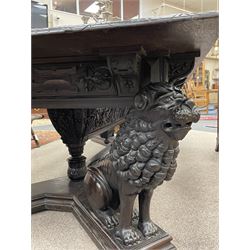 Large 19th century carved oak library table, the rectangular top with lunette carved edge over cartouche panelled and carved  scroll frieze, the central tapering rectangular support relief carved with masks and garlands, on four carved seated lion supports at each corner, on flat angular stretcher with recessed castors stamped ‘Bartholomew & Fletcher, London’