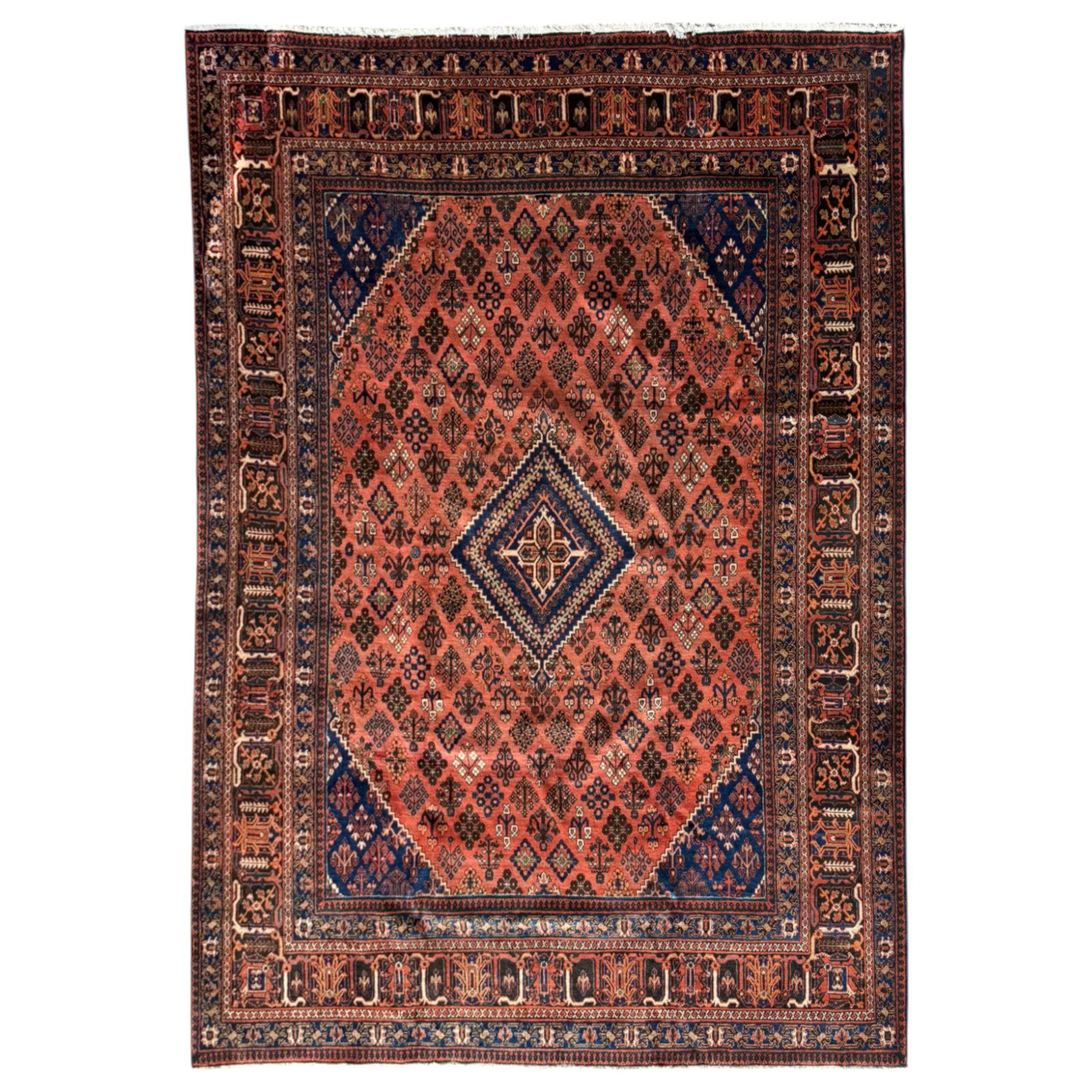 Joshgan Persian wool rug, with diamond-framed medallion, on a deep red field filled with geometric-shaped floral motifs and indigo-filled spandrels 