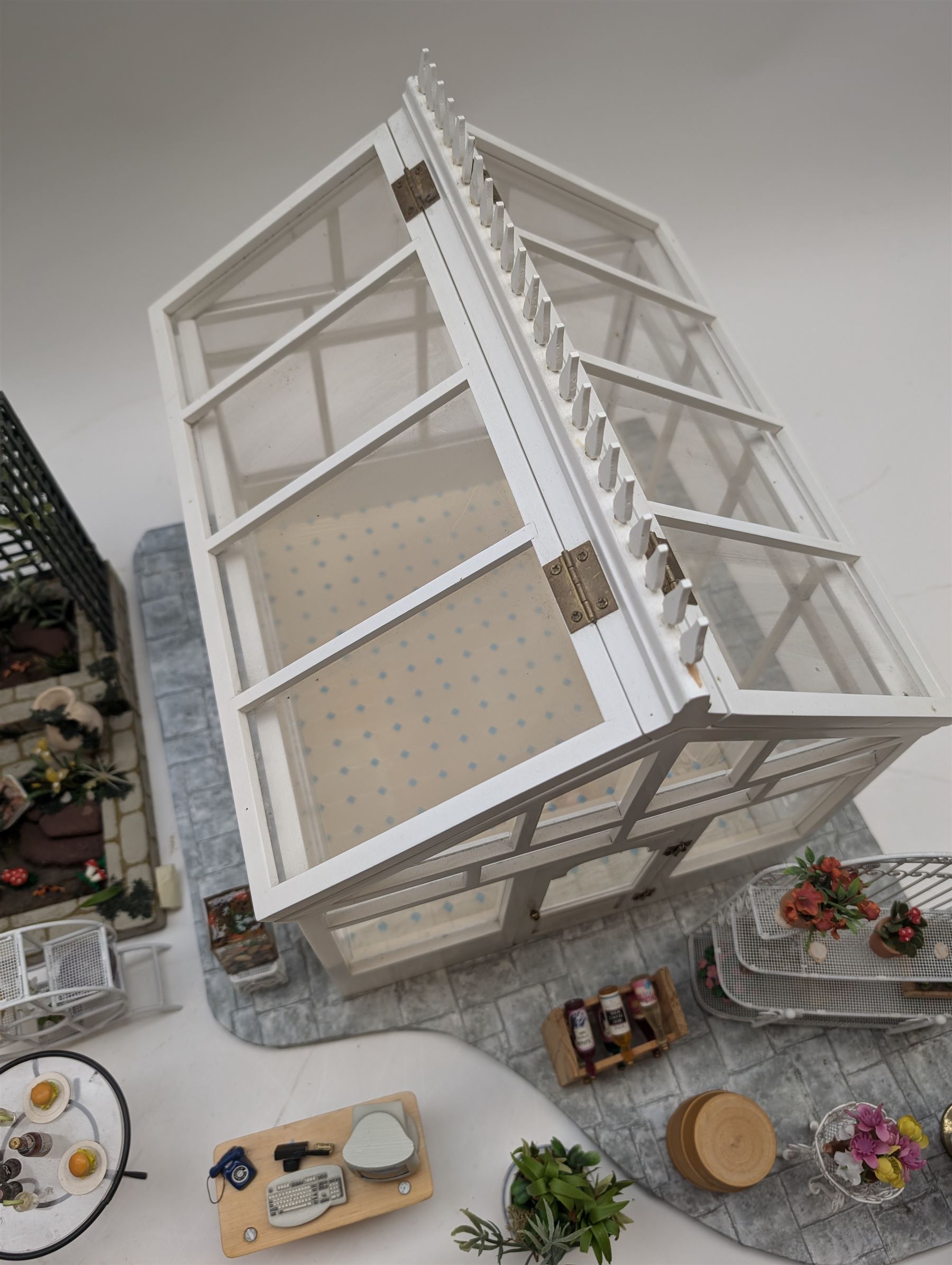 1:12 scale dolls house conservatory and garden accessories, including white wooden glazed conservatory on a stone effect base, black and white metal garden seating, barbecue, plant shelves, parasol, barbeque accessories, large planters, rabbit hutch, animals, chimenea, etc