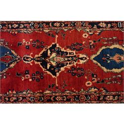 Persian Hamadan runner rug, the vermilion ground decorated with a row of ivory and indigo medallions interspersed with stylised flowering plants, indigo spandrels, enclosed by an indigo floral border and narrow patterned guard stripes