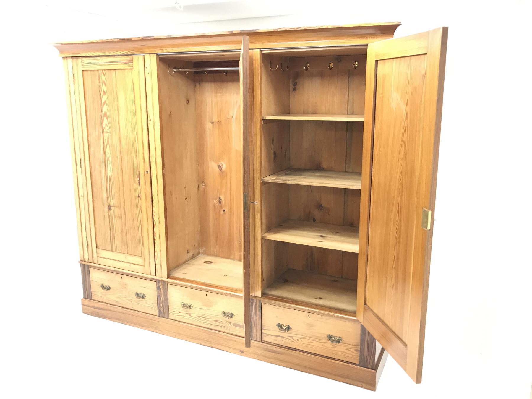 Late Victorian large pitch pine triple wardrobe, projecting cornice, central mirrored door flanked by two others above three drawers, plinth base