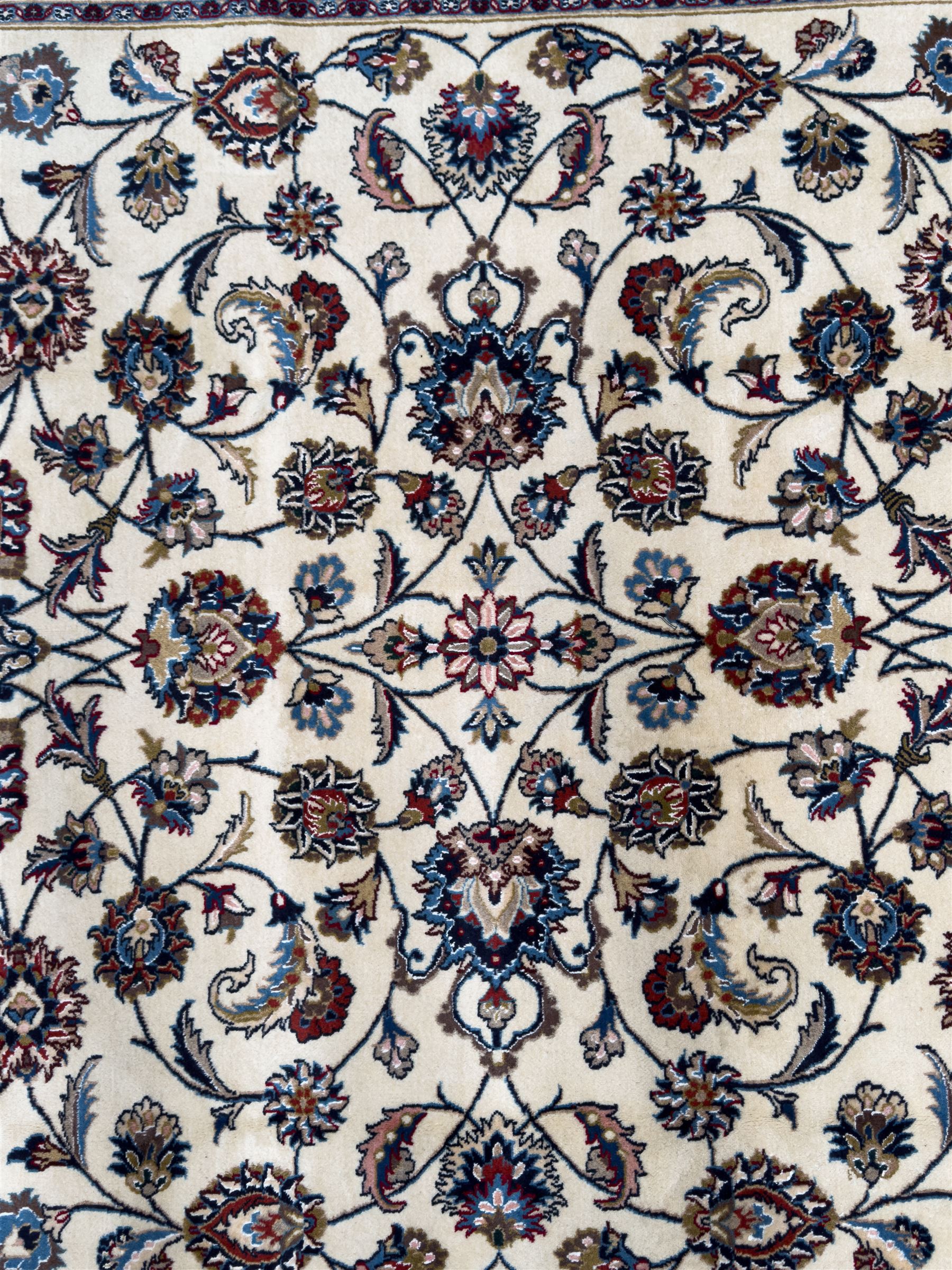 Northeastern Persian Meshed hand-knotted rug, ivory ground with an overall design of scrolling vines, palmettes, and rosettes in an indigo palette, soft blues, and madder, framed by a deep indigo border of lotus palmettes and flowerheads between multiple guard borders, 300cm x 202cm