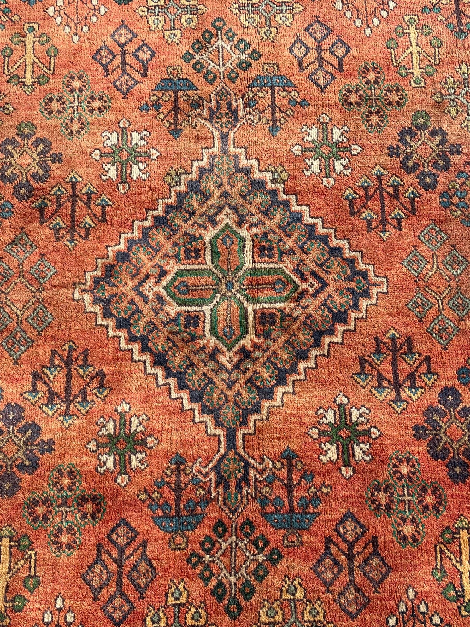 Persian Joshaghan rust ground rug, stepped lozenge medallion surrounded by repeating foliate lozenge motifs, the border decorated with stylised plant motifs, within geometric guard stripes
