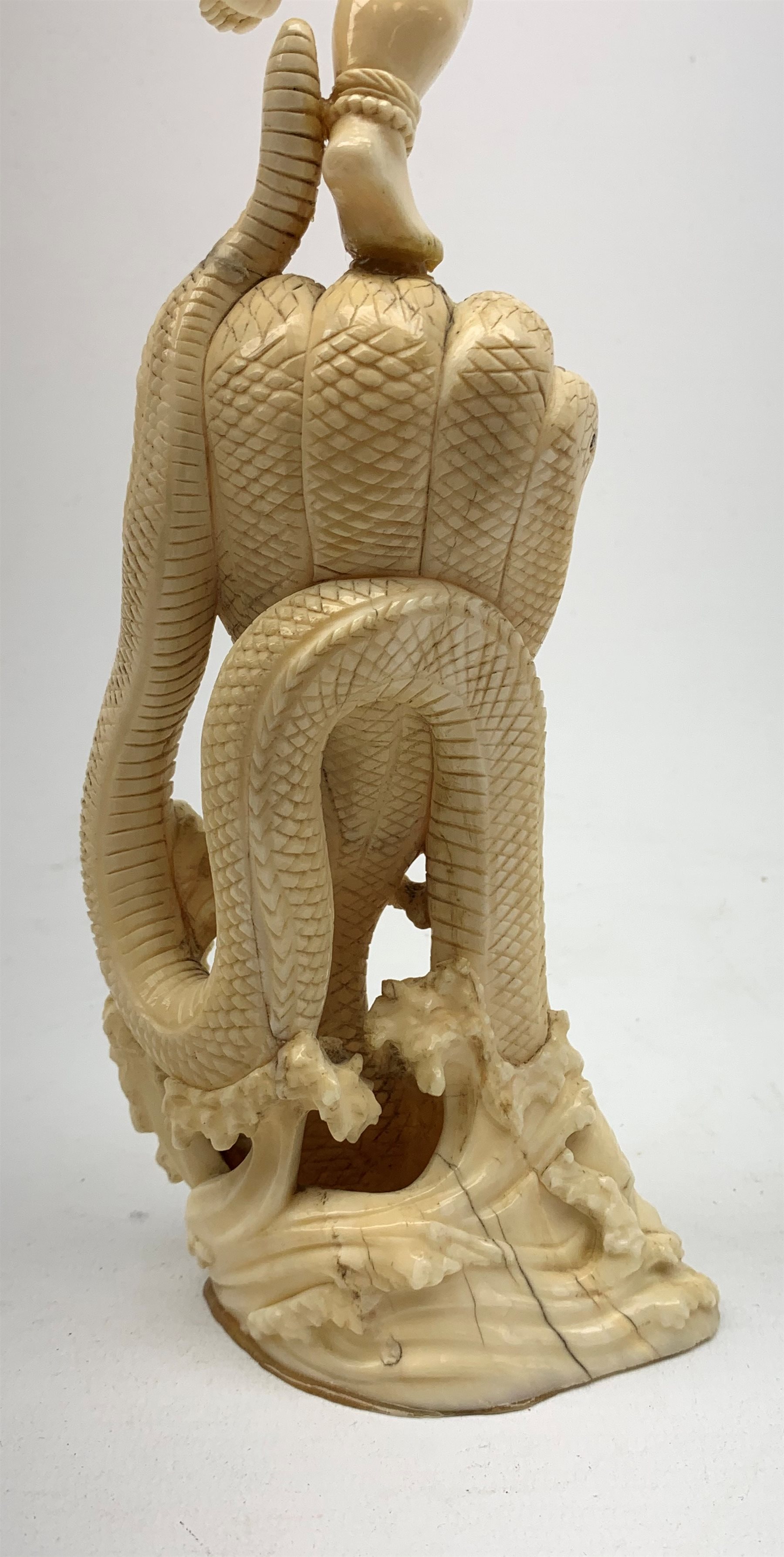 A large Japanese carved ivory okimono, modelled as a figure stood upon one leg with arms outstretched, upon a five headed serpent emerging from waves, H30cm.